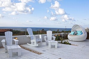 Une terrasse sur le toit avec des fauteuils Adirondack blancs, un canapé en osier blanc et une vue sur l’océan.