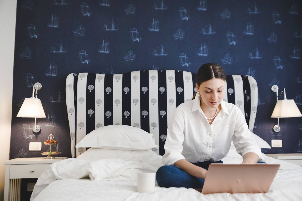 A hotel room with a bed, a laptop, and a nightstand with a lamp and a small table with a fruit plate.