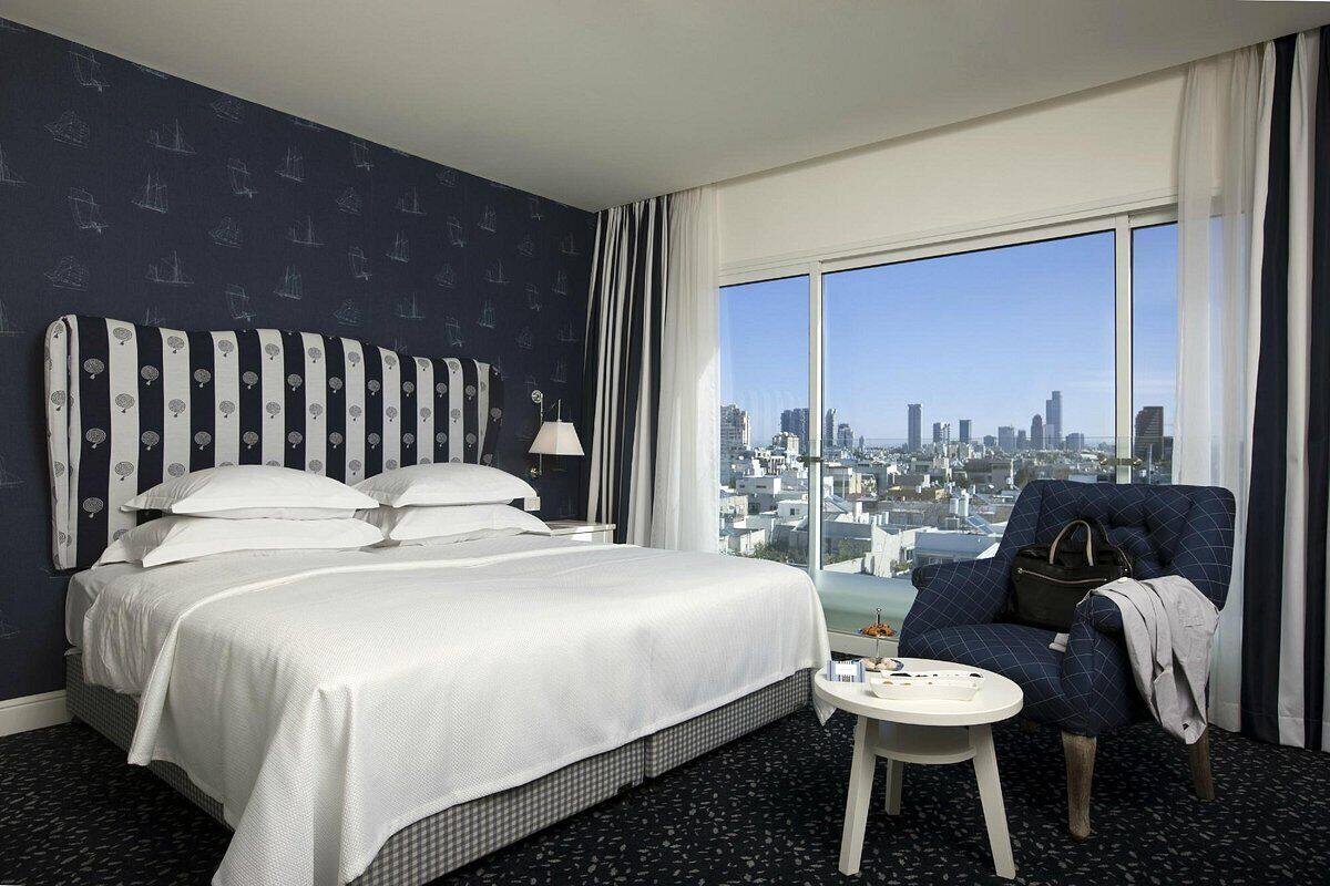 A hotel room with a large bed, a chair, a small table, and a city view.