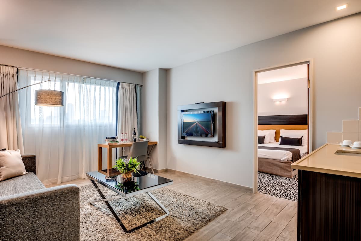 A modern hotel room with a sofa, a coffee table, a TV, and a bed.