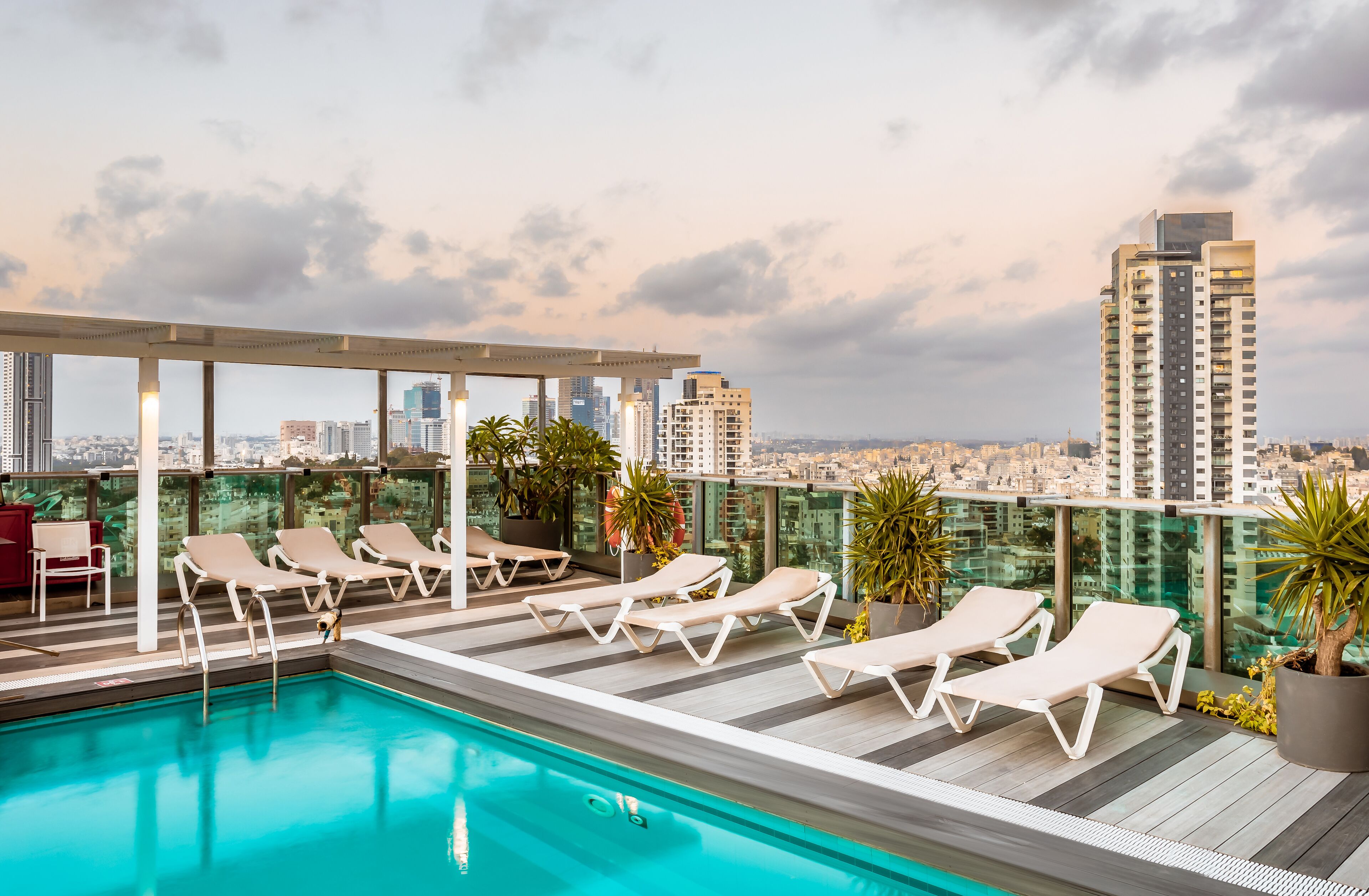 Une piscine sur le toit, agrémentée de chaises longues et de plantes en pot, offrant une vue panoramique sur la ville.