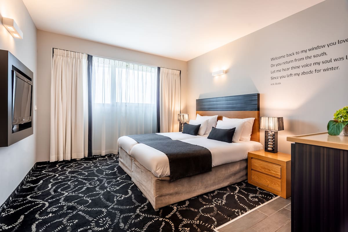 A modern hotel room with a large bed, bedside lamps, a desk, and a view of the outdoors.