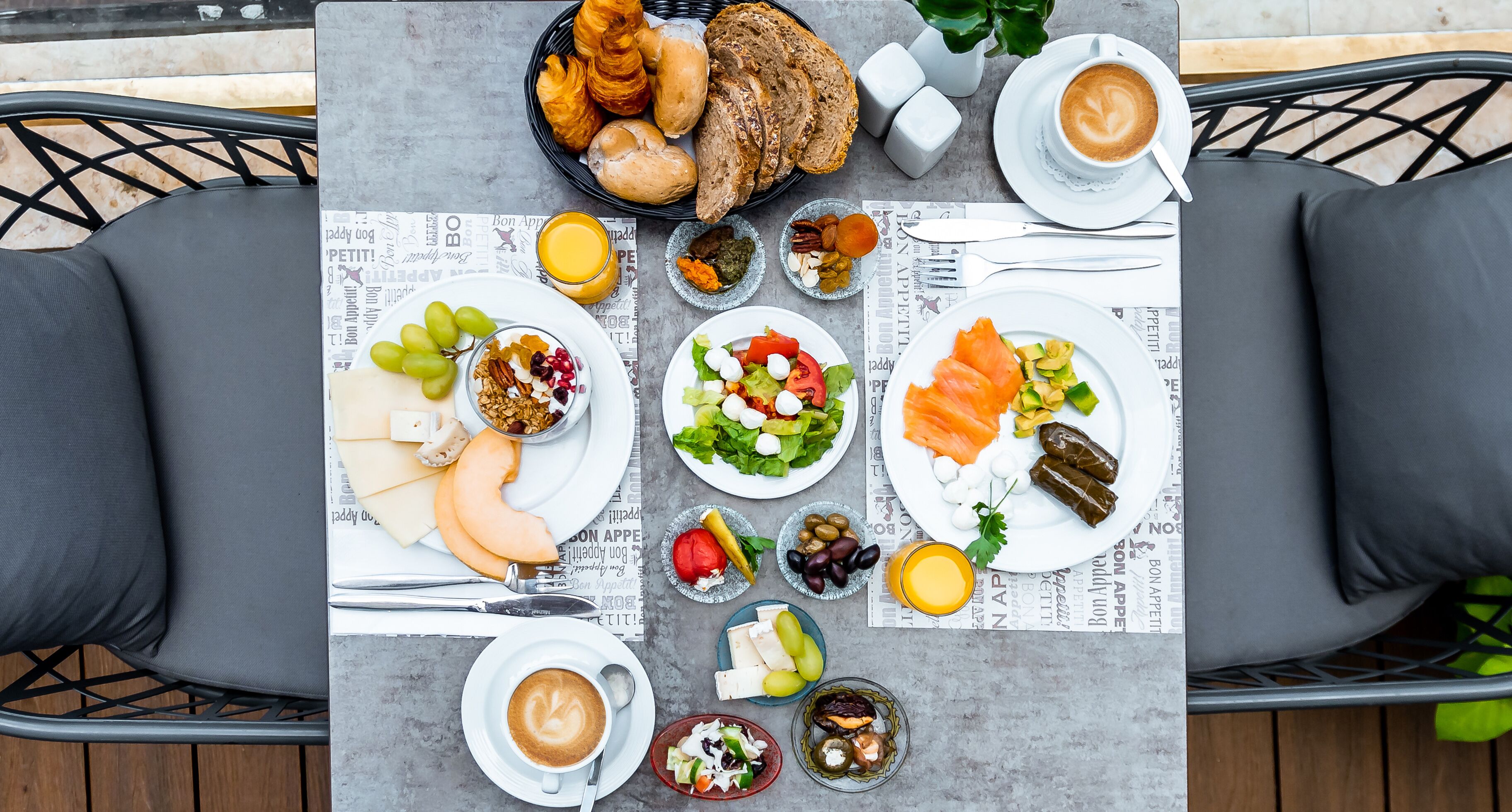 A table set with various breakfast items including bread, pastries, fruits, and beverages, with a newspaper underneath.