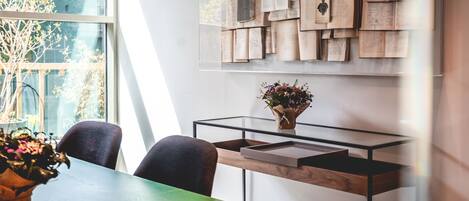 A modern room with a glass table, two chairs, a vase with flowers, and a wall decorated with papers and books.