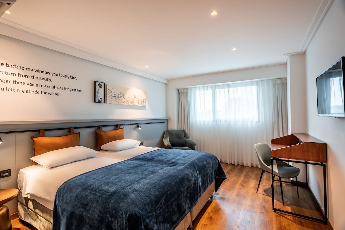 A modern hotel room with a large bed, a desk, and a chair.