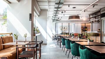 En moderne restaurant med en lang disk, båsestole og grønne stole. Der er planter på bordene og et stort vindue til venstre.