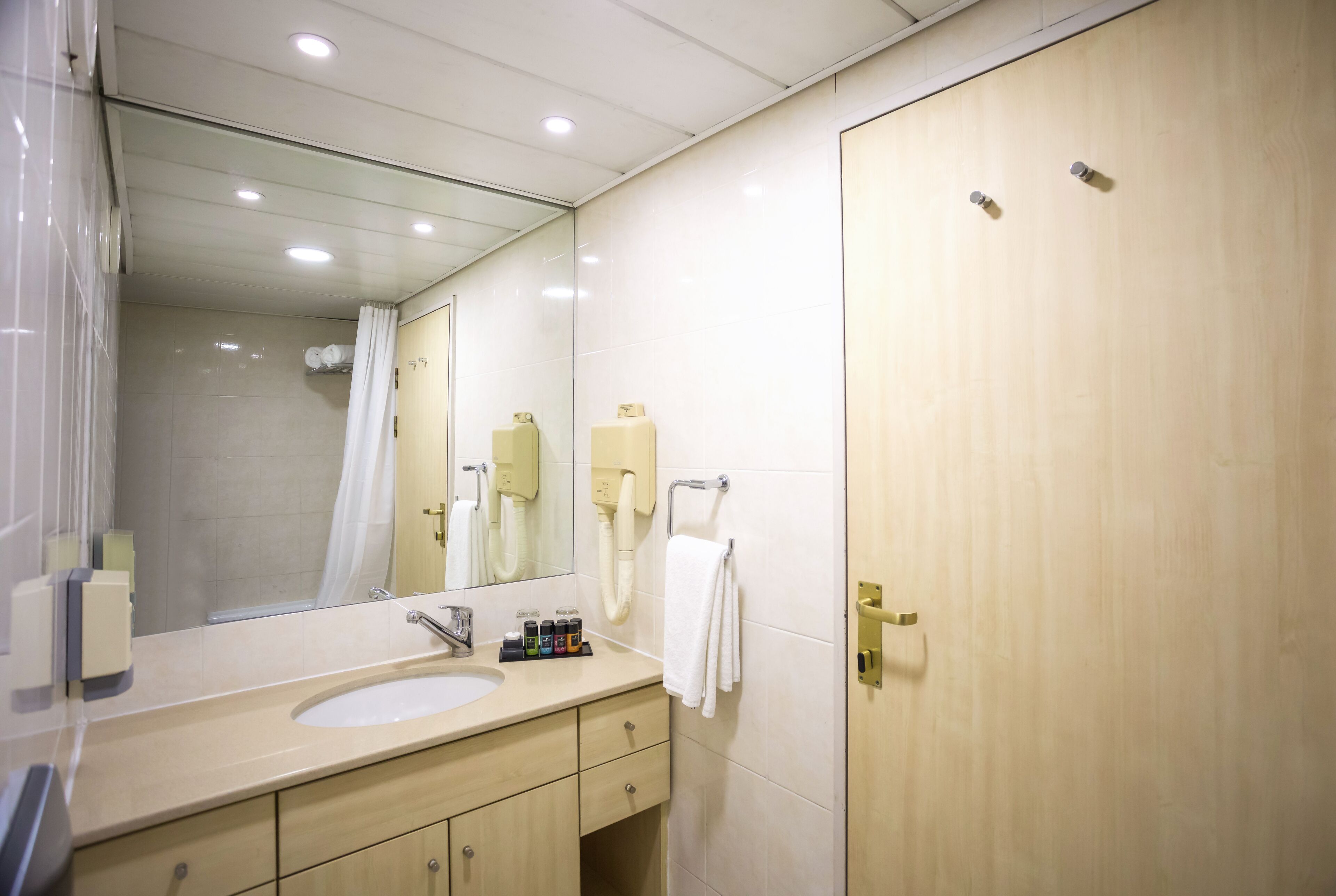 Un baño con lavamanos, espejo, toallero y puerta.