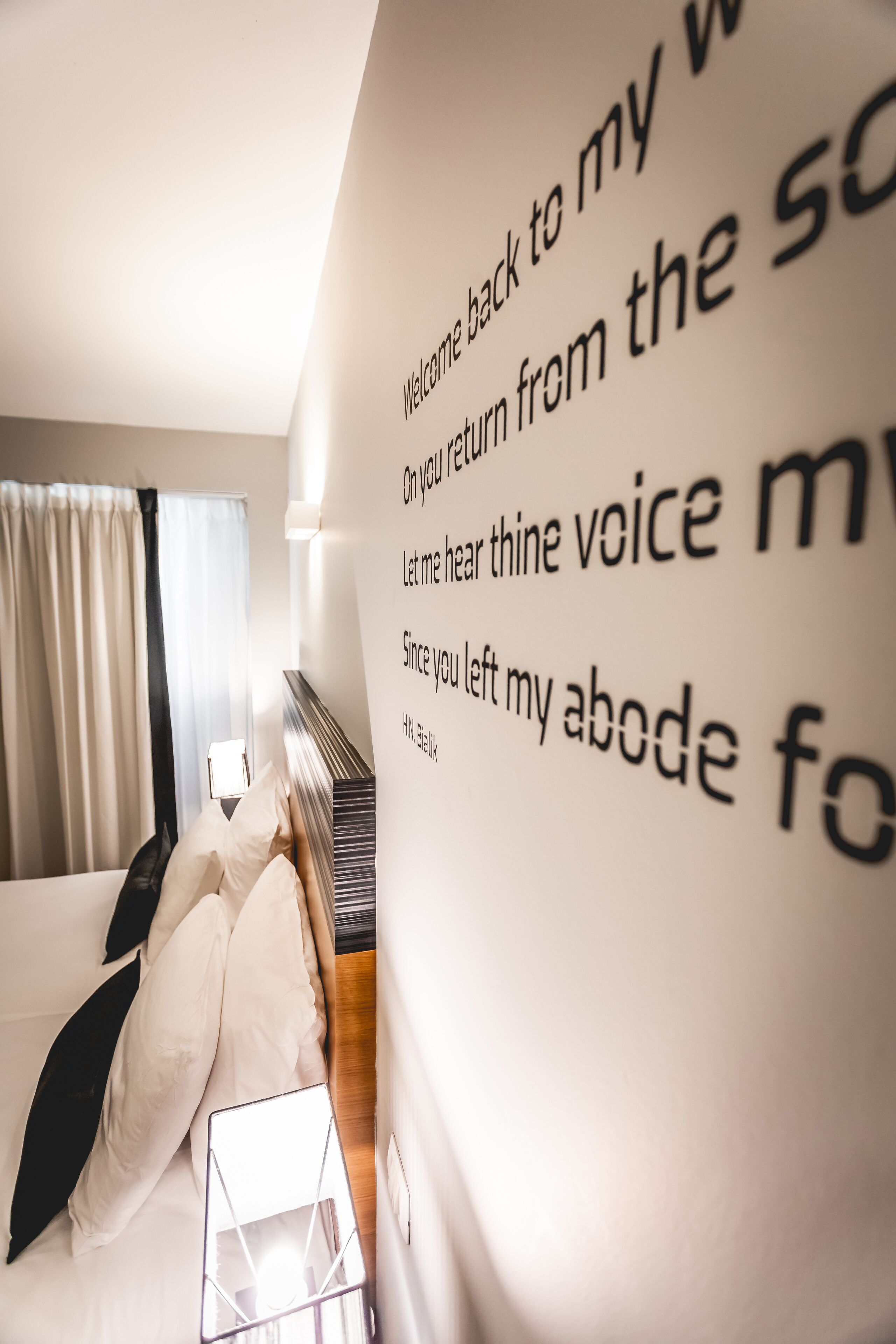 Una habitación de hotel con una cama, almohadas, una mesita de noche y una pared con texto.