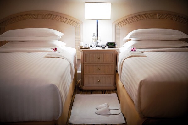 A hotel room with two beds, a nightstand with a lamp, a clock, and a bottle of water.