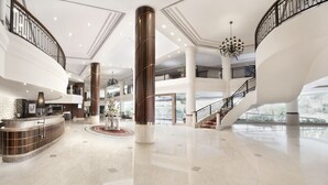 Un hall d’entrée spacieux avec un comptoir de réception, de grandes colonnes, un escalier et un lustre.