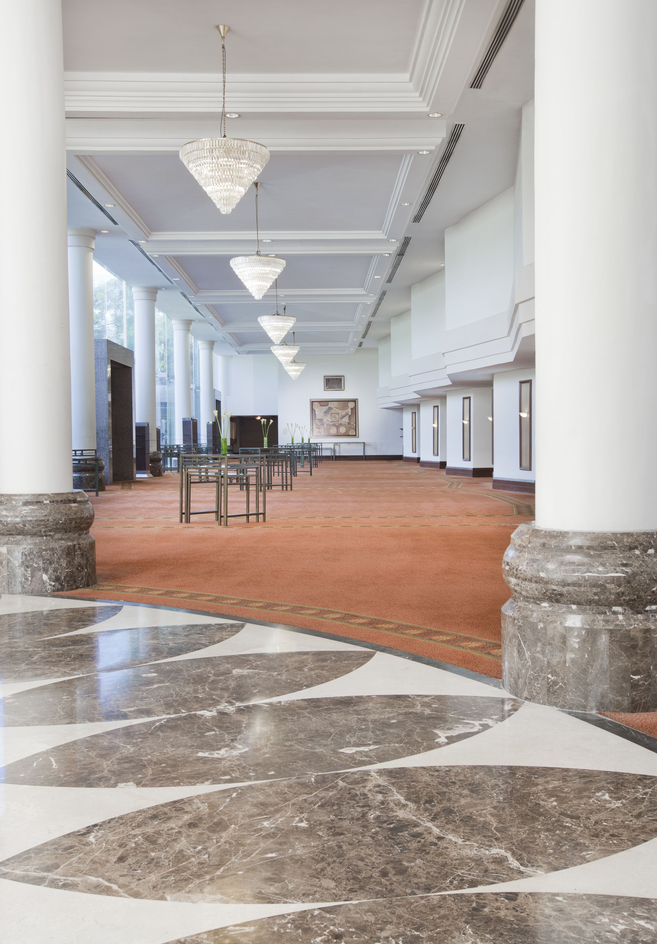 Eine geräumige Lobby mit Marmorboden, großen Säulen und hängenden Kronleuchtern.