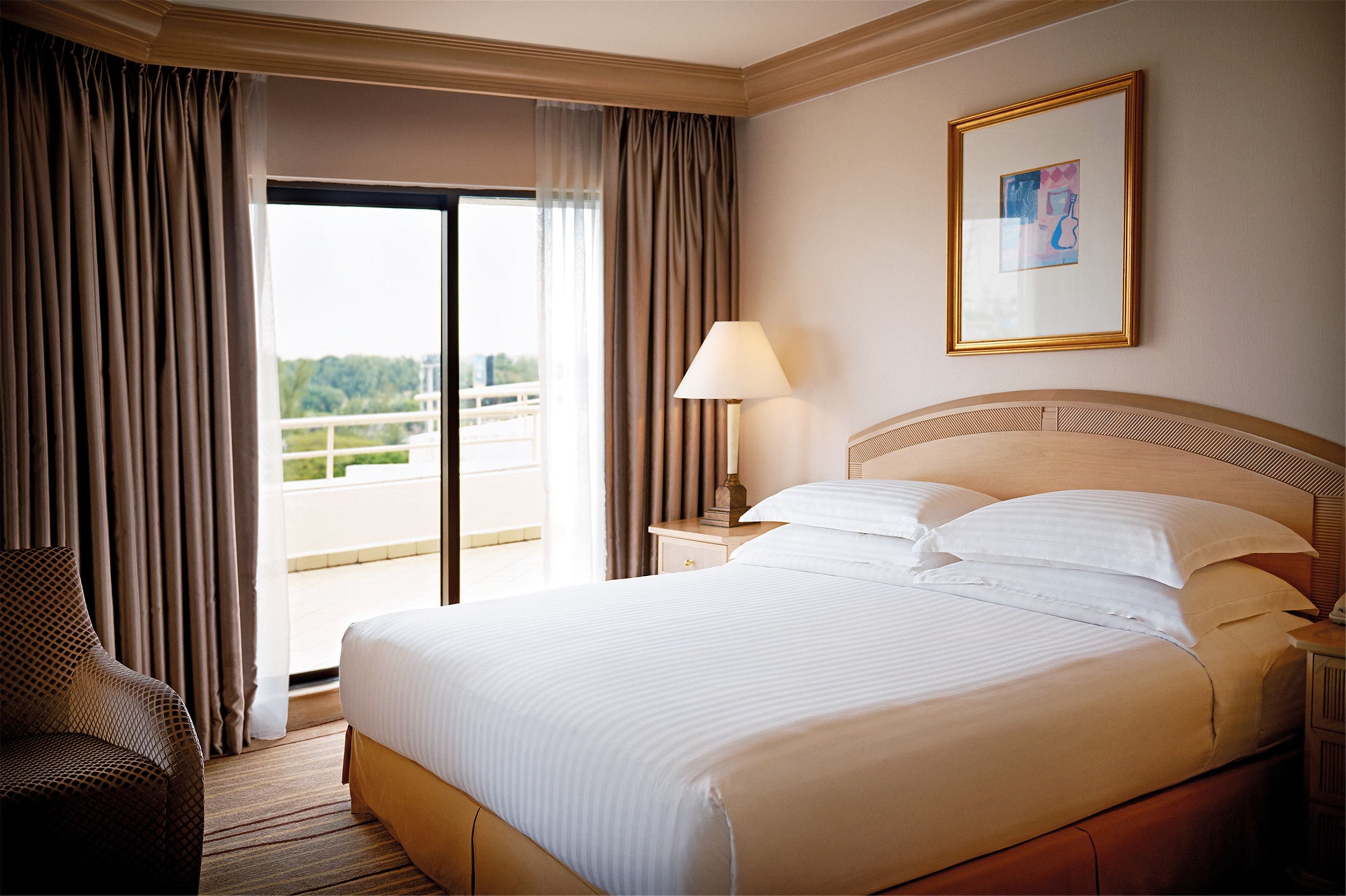 A hotel room with a large bed, a chair, a nightstand, a lamp, and a window with curtains.