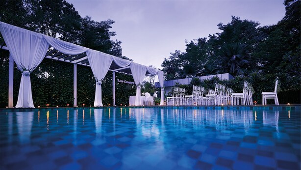 Une piscine extérieure au motif à carreaux, entourée de parasols blancs et de chaises blanches.