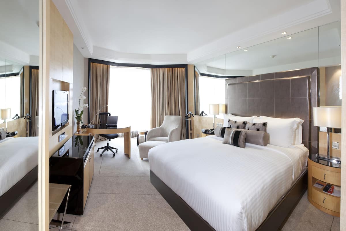 A hotel room with two beds, a desk, a chair, a TV, and a mirror.