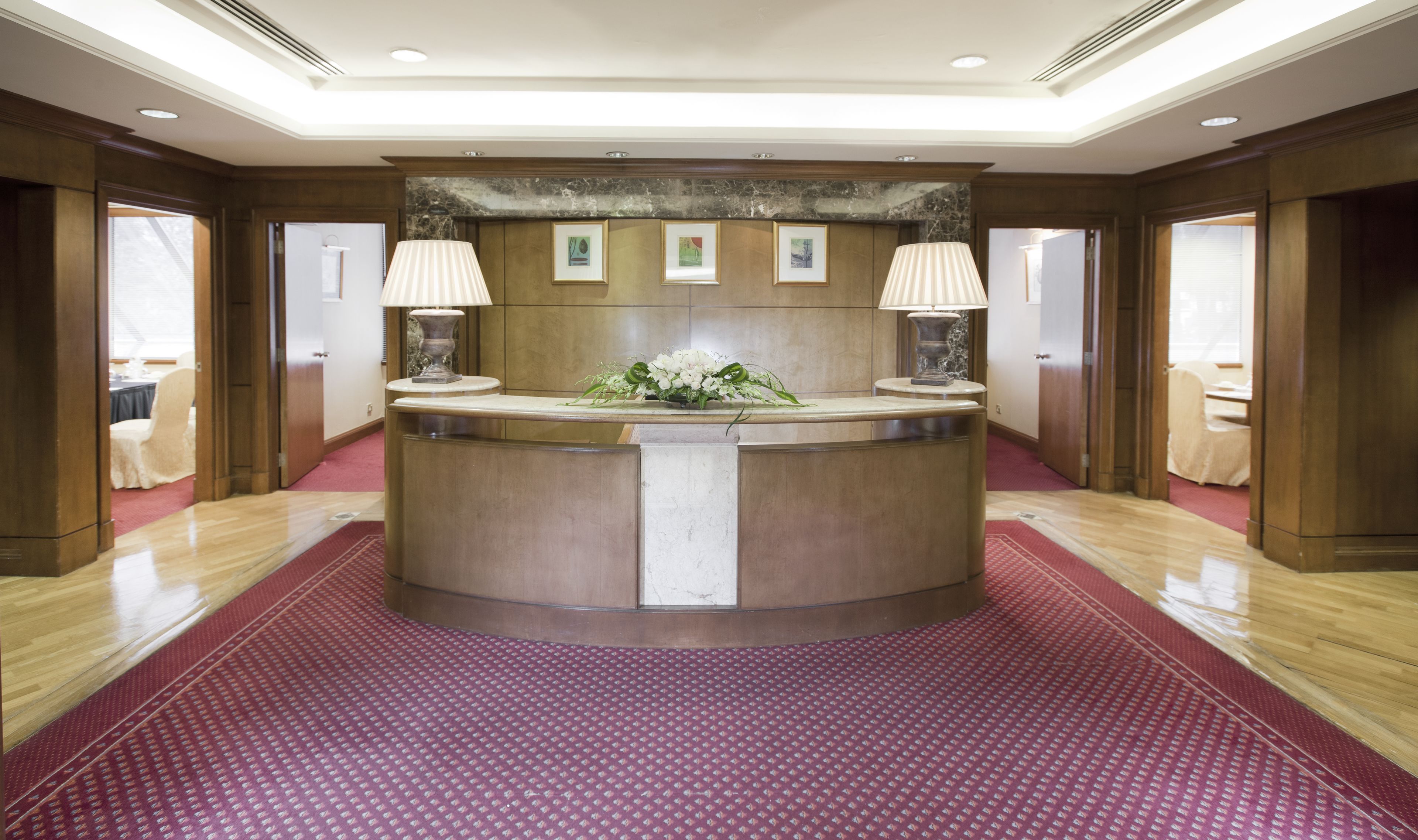 A reception area with a marble counter, two lamps, framed artwork, and a red patterned carpet.