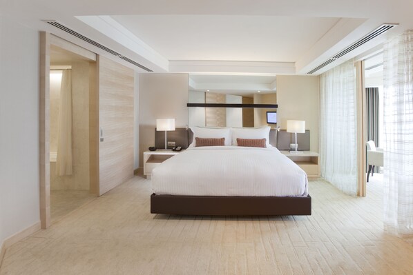 A modern hotel room with a large bed, bedside tables with lamps, a TV, and a view of the city through large windows.