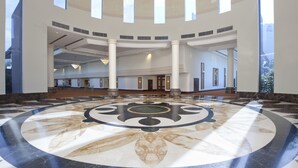 Un hall d’entrée spacieux doté d’un sol circulaire en marbre, de hauts plafonds percés d’une verrière et de grandes fenêtres laissant entrer la lumière naturelle.