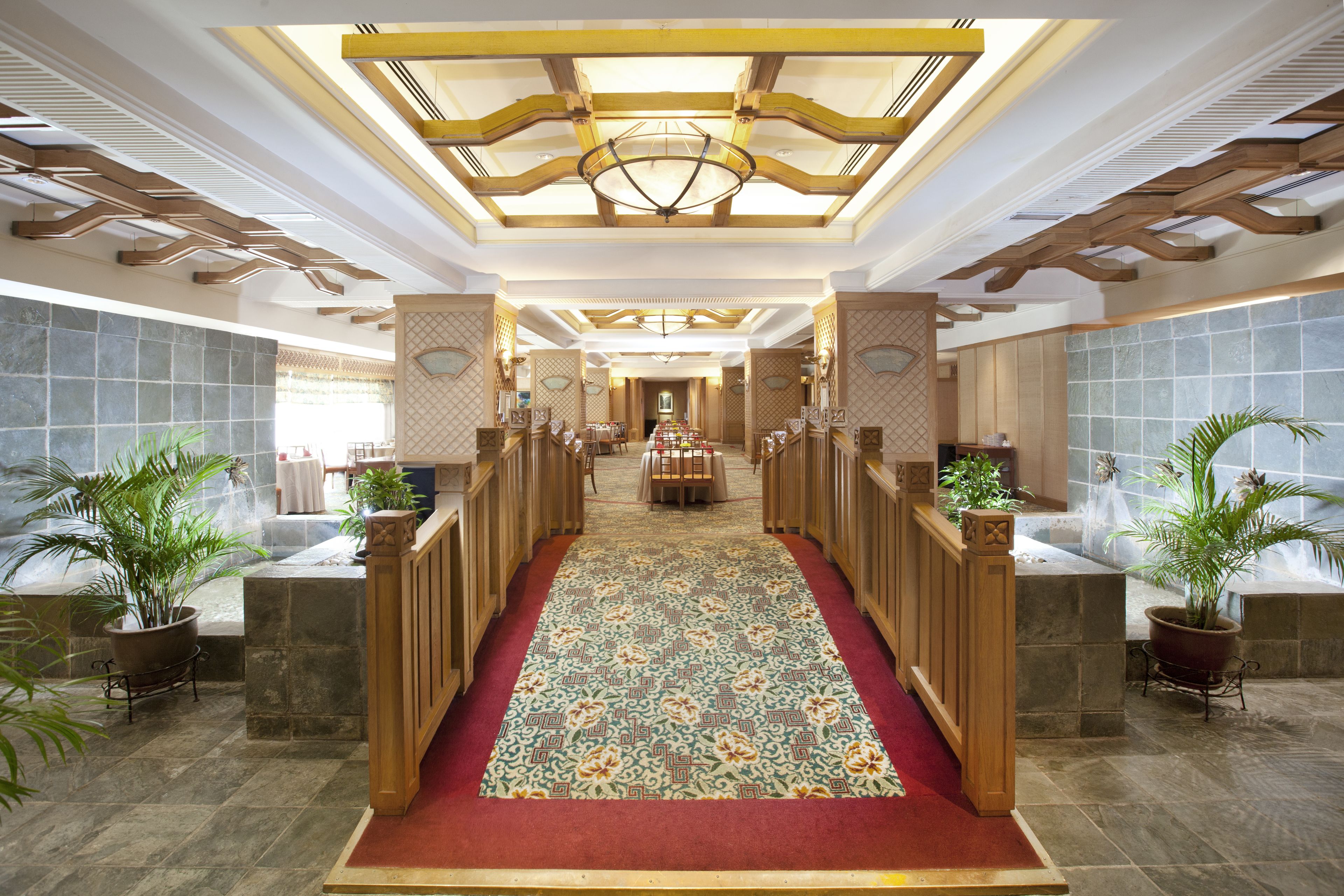 A hotel lobby with a red carpet, wooden railings, and potted plants.