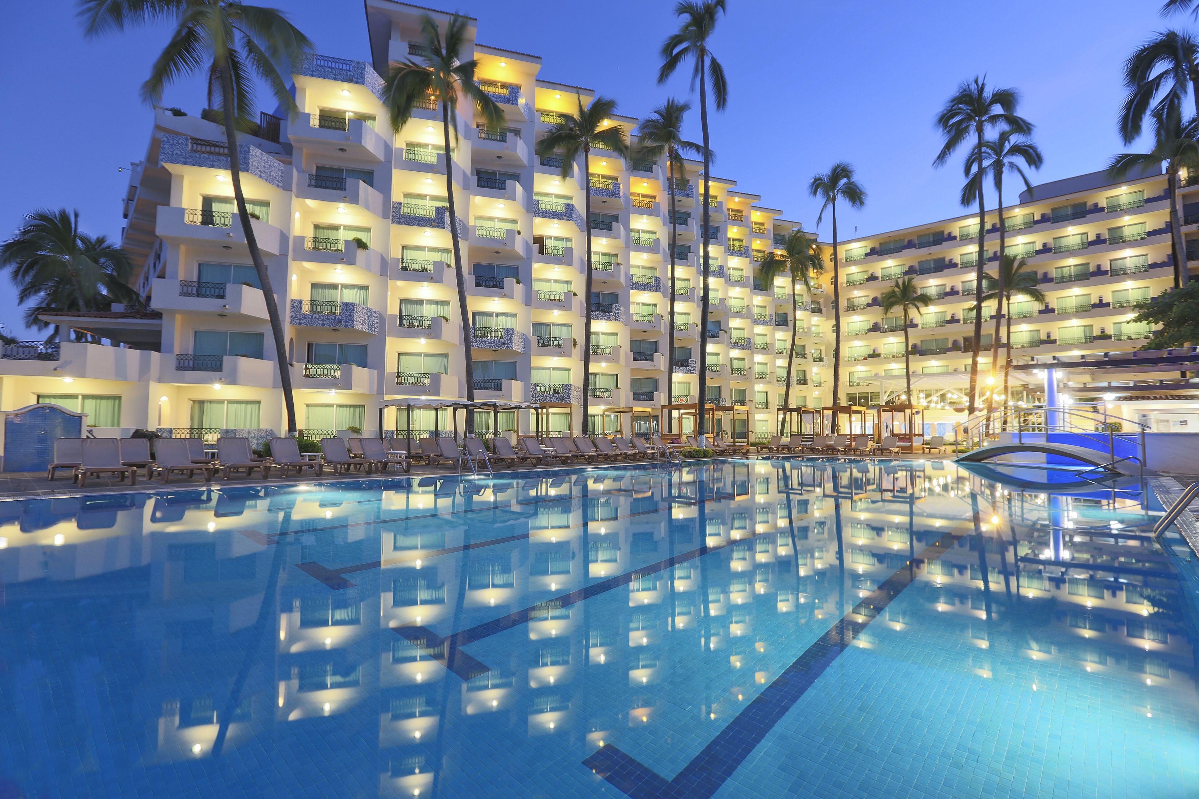 Ein Hotel mit einem großen Schwimmbecken, mehreren Balkonen und Palmen.