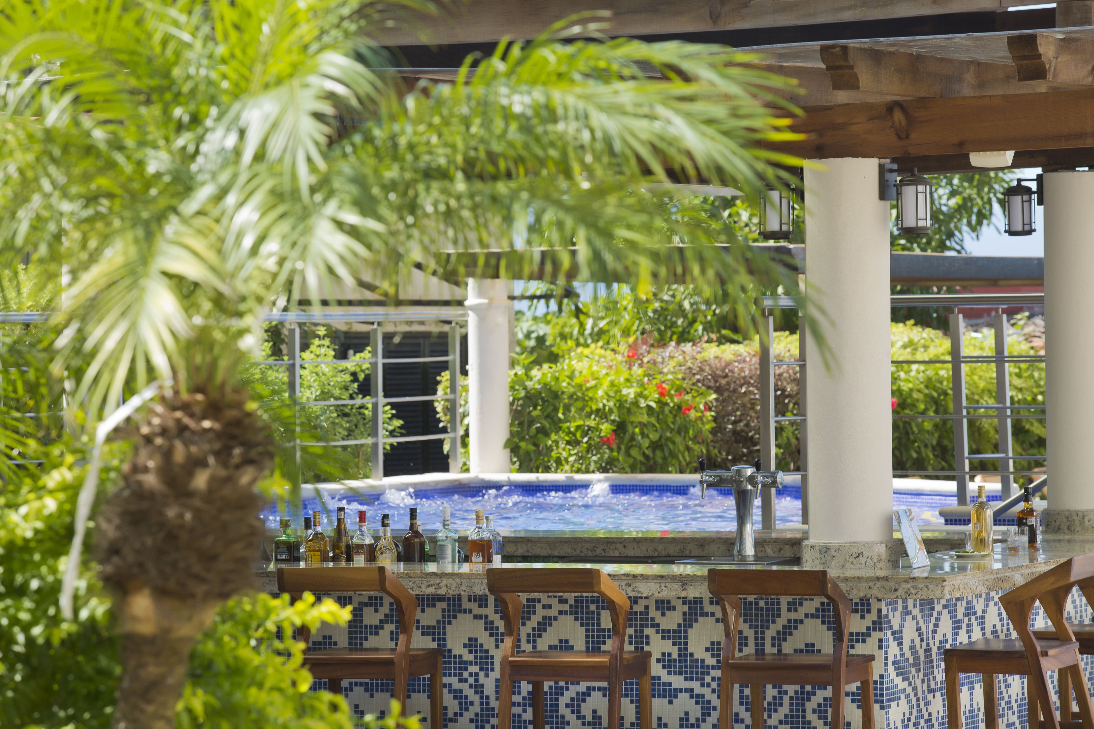 Zona de bar con salpicadero de azulejos, sillas de madera y una piscina al fondo.