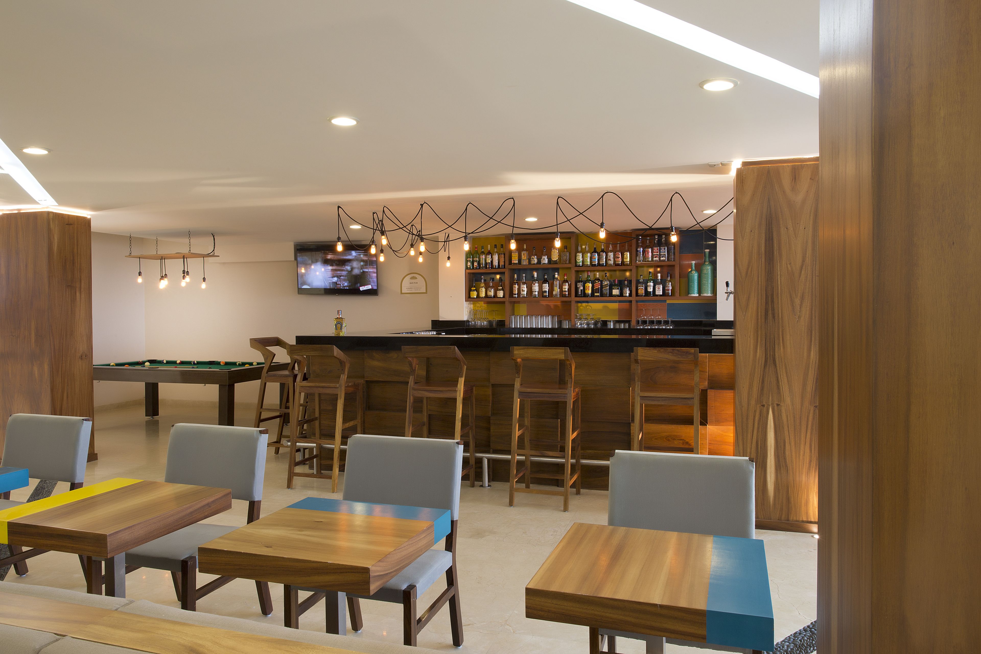 Zona de bar con mobiliario de madera, mesa de billar y una pantalla de televisión.
