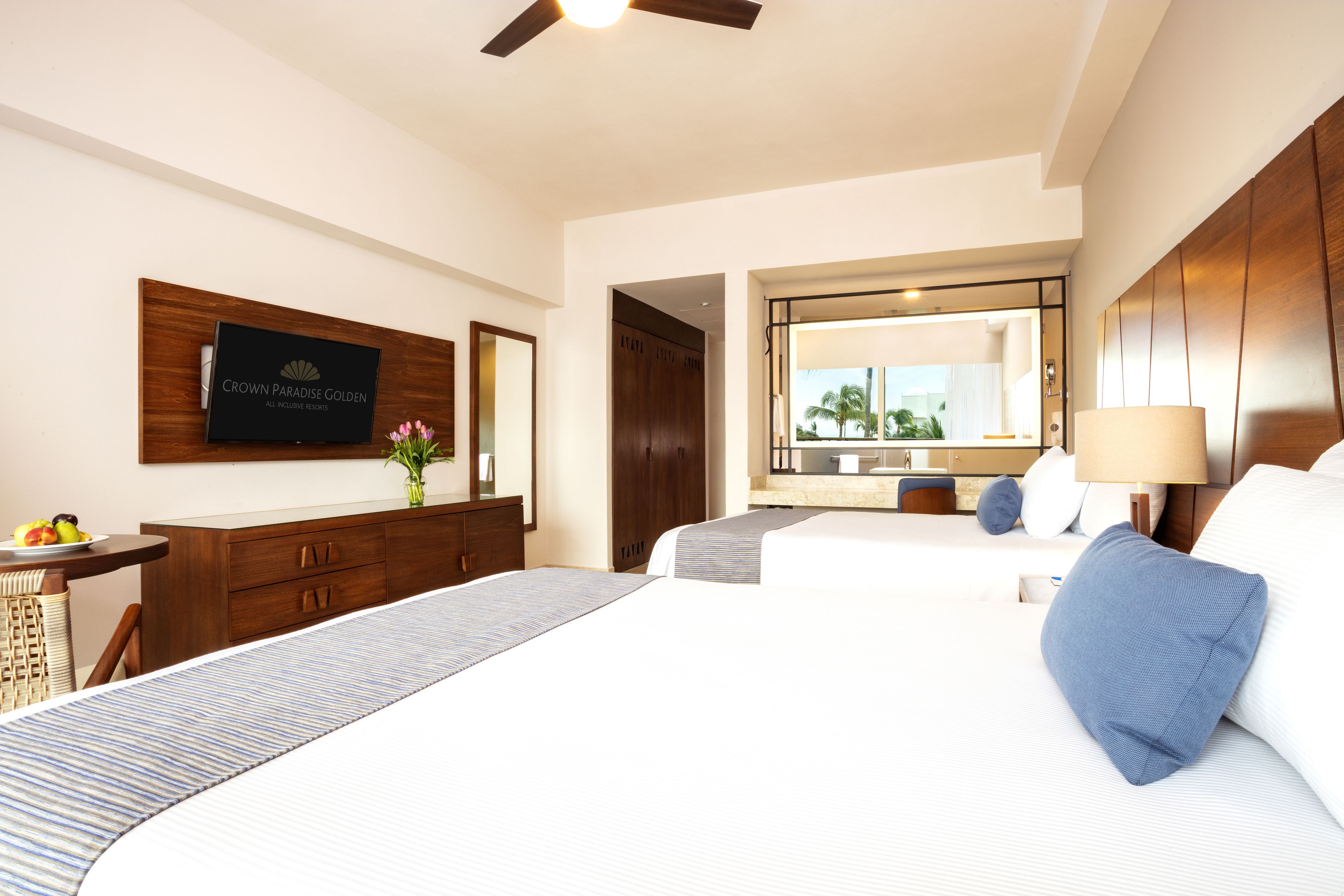 A hotel room with a large bed, a desk with a computer, a mirror, and a television on the wall.