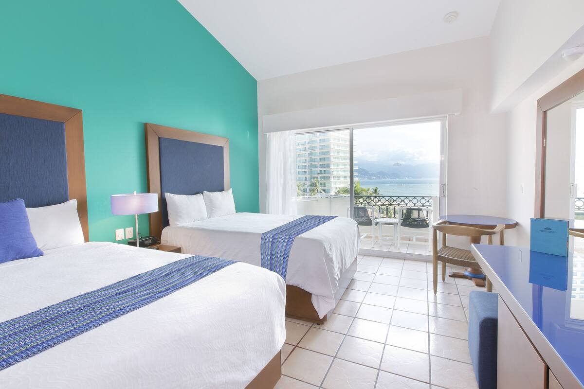 Une chambre d’hôtel avec deux lits, un balcon avec vue et un bureau.