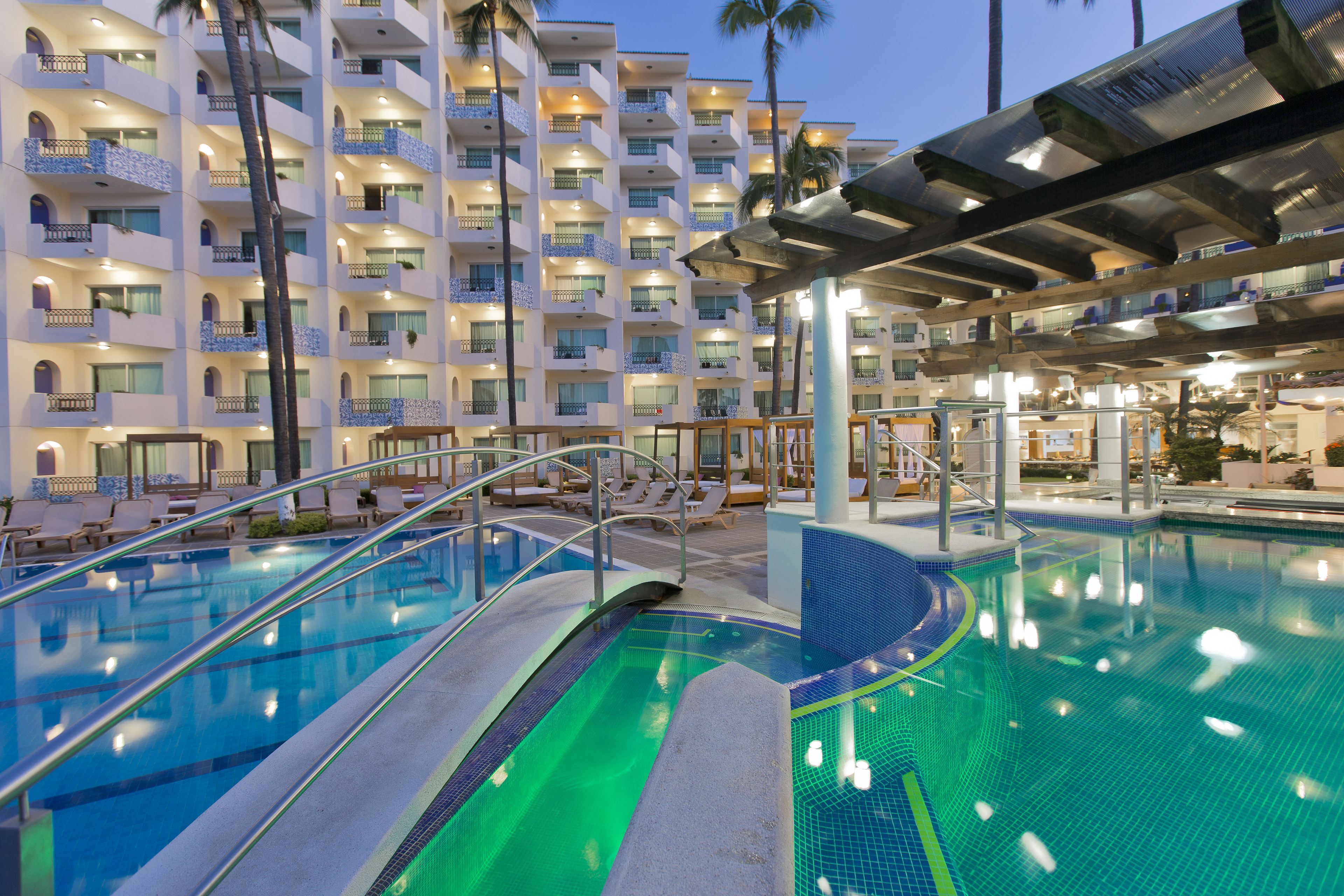 A hotel pool area with multiple levels of balconies, lounge chairs, and a covered seating area.