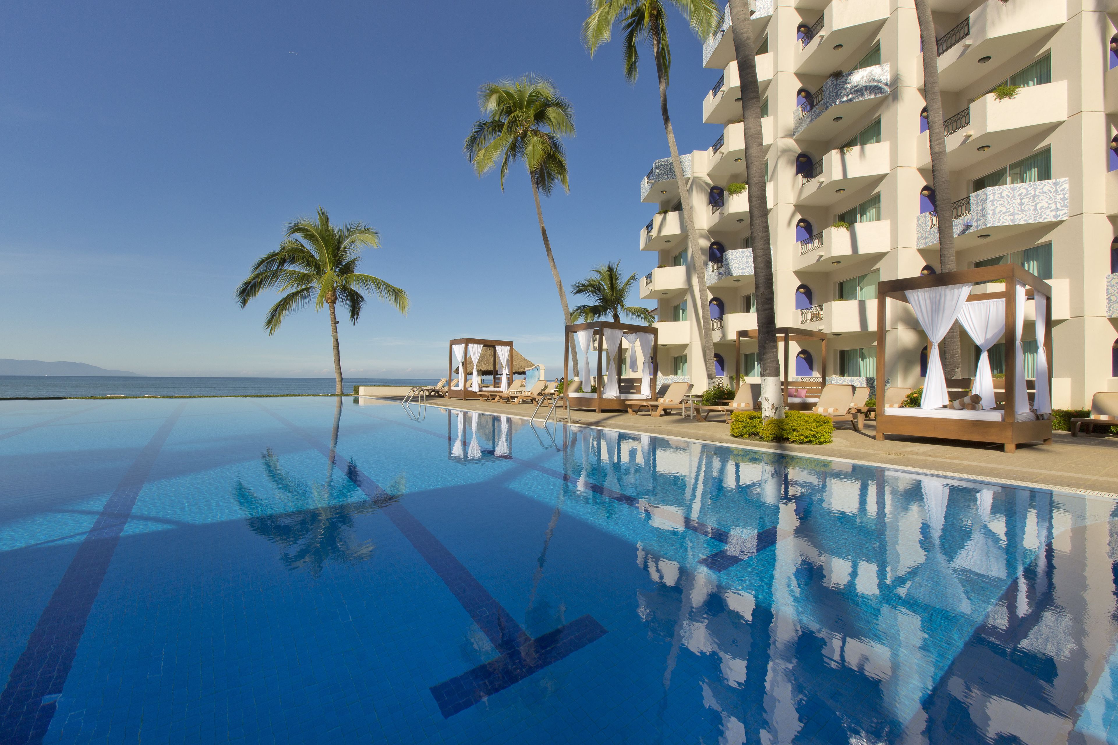 Una piscina de hotel con agua azul cristalina, palmeras y vistas al océano.