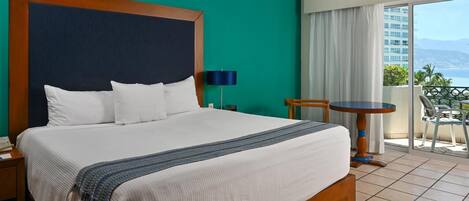 Una habitació d'hotel amb un llit gran, una taula petita i un balcó amb vistes.