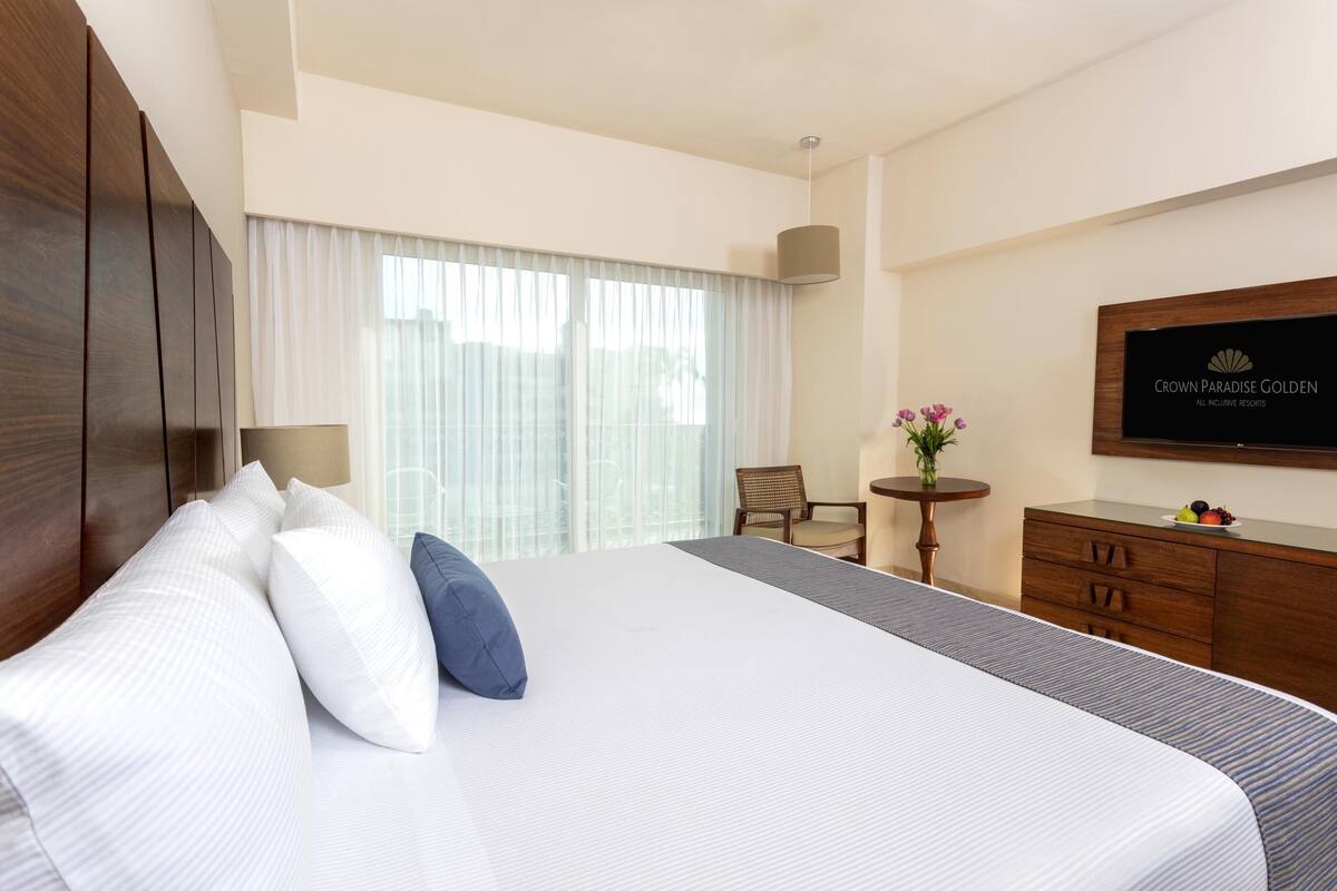 Une chambre d’hôtel avec un grand lit, un bureau, une chaise, une petite table ornée de fleurs et un téléviseur fixé au mur.