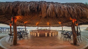 Ein Restaurant direkt am Strand mit einem Reetdach, Terrassenplätzen und einer zentralen Bar.