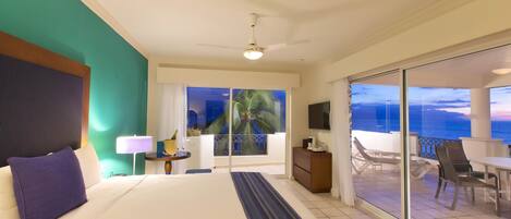 A hotel room with a bed, a nightstand, a lamp, a view of the ocean, and a balcony with chairs.