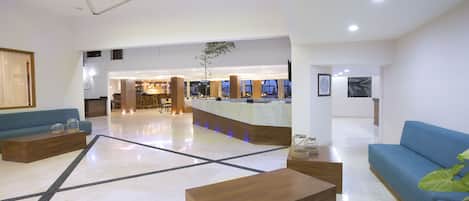A spacious lobby with a reception desk, seating areas, and a large plant.