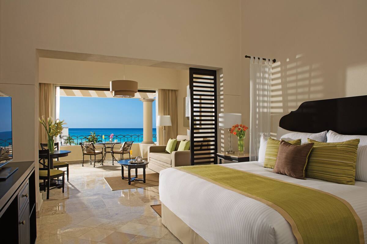 Hotelkamer met een groot bed, een balkon met uitzicht op zee, een zithoek en een televisie.