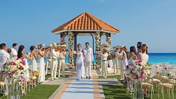 A wedding ceremony on a beach with a gazebo, guests, and floral decorations.