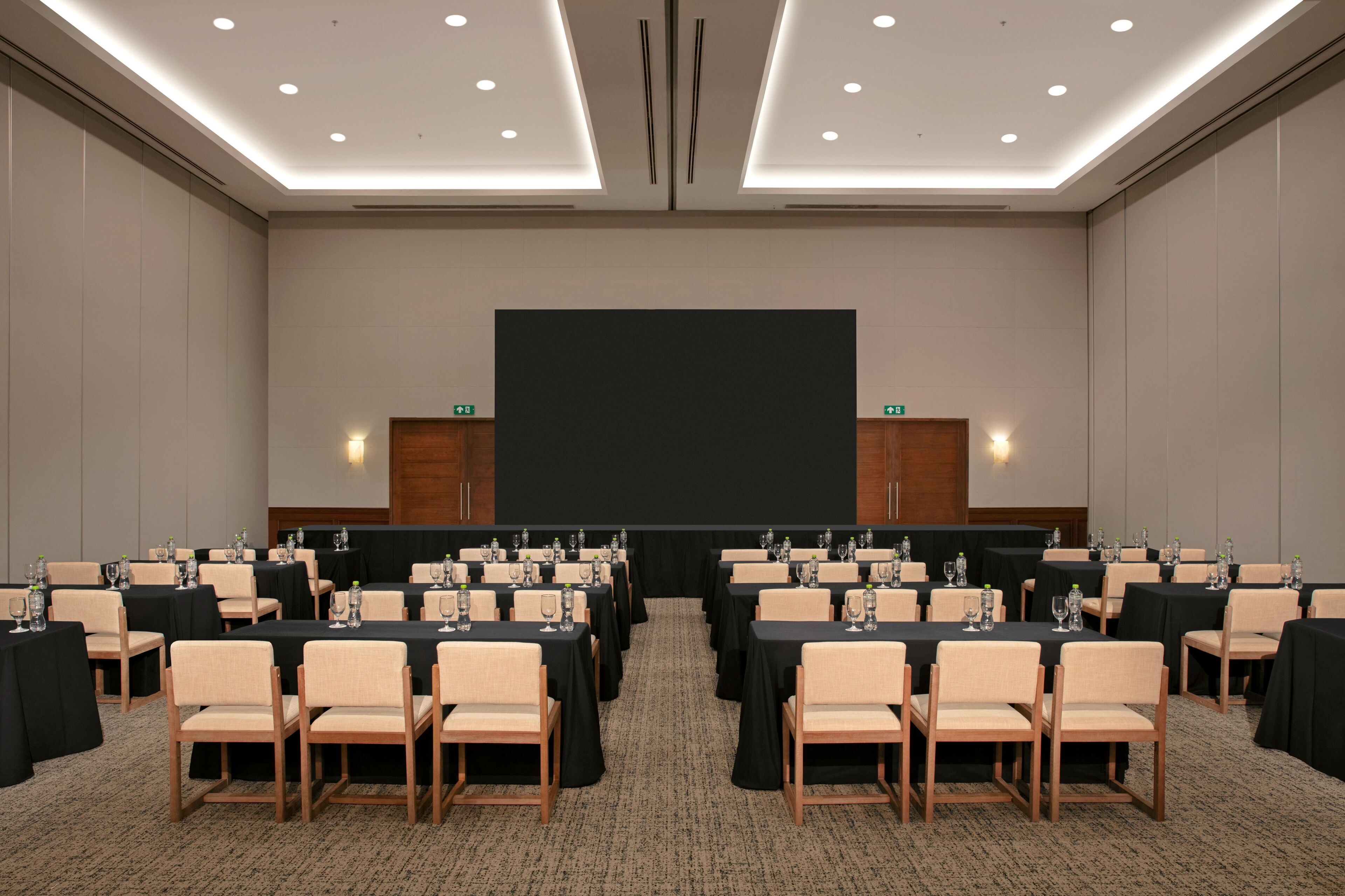 A conference room with multiple tables, chairs, and a large screen at the front.