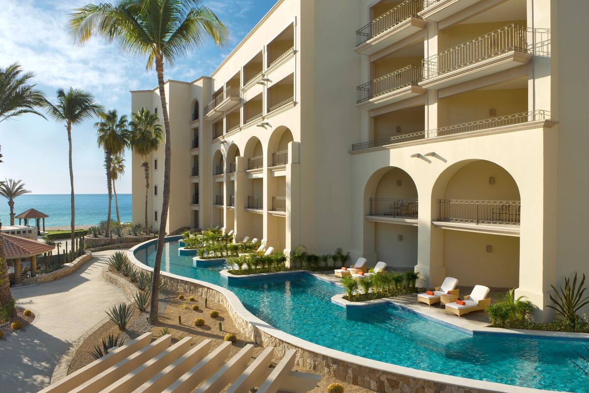 Een resort met een zwembad, palmbomen en uitzicht op de oceaan.