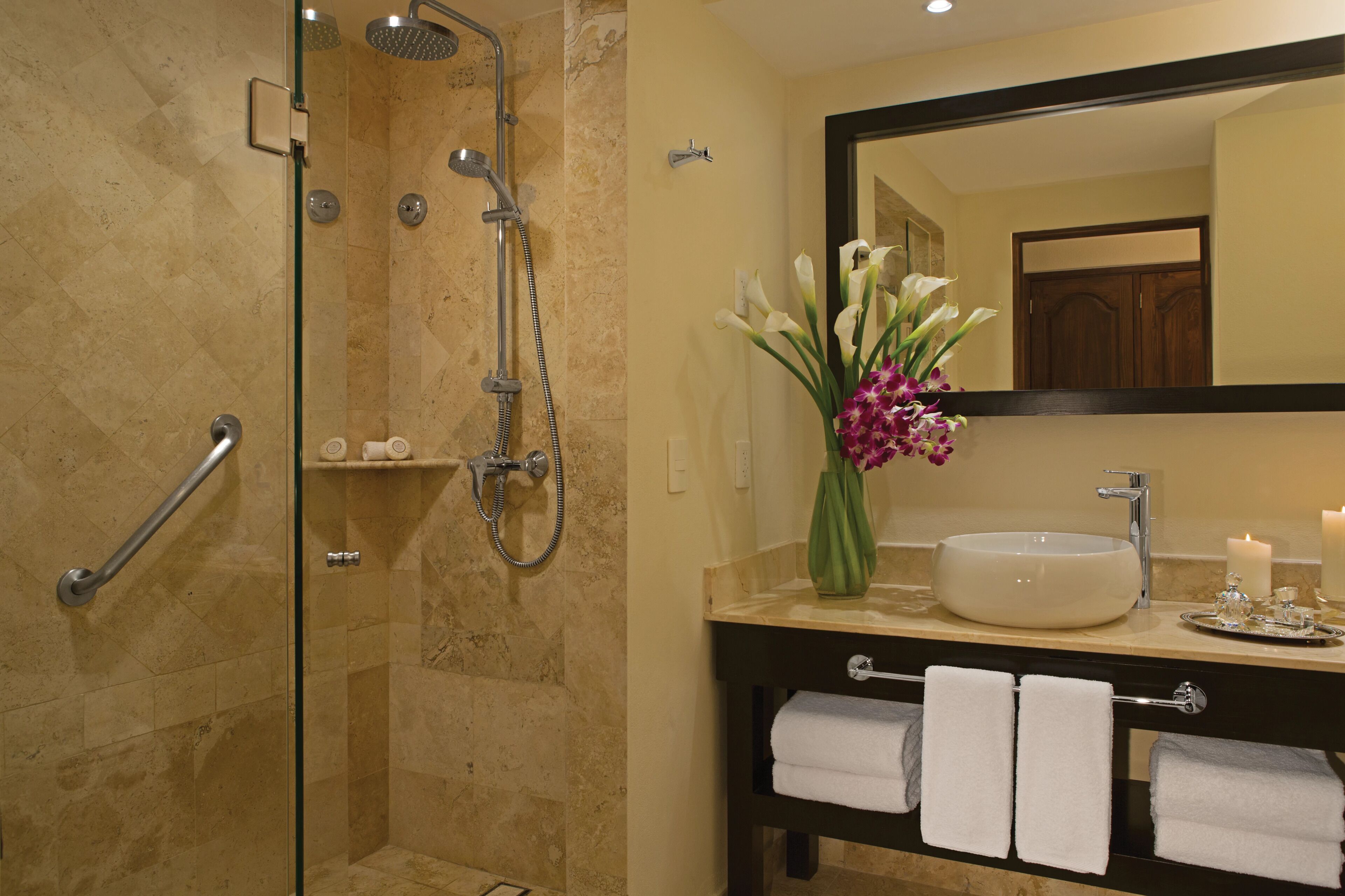 A bathroom with a glass-enclosed shower, a vanity with a sink, and a mirror.