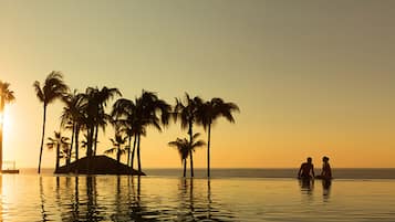 A sunset view with palm trees and a couple in a pool.