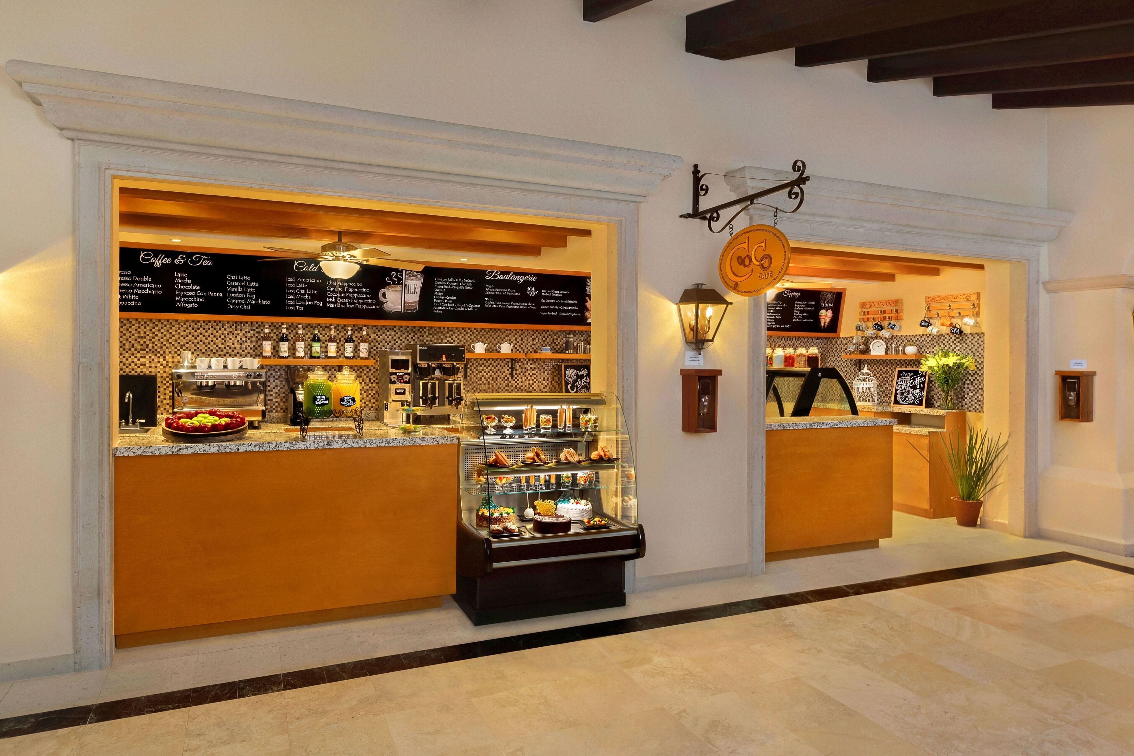 Un café avec un tableau affichant le menu, une vitrine remplie de pâtisseries et une enseigne suspendue.
