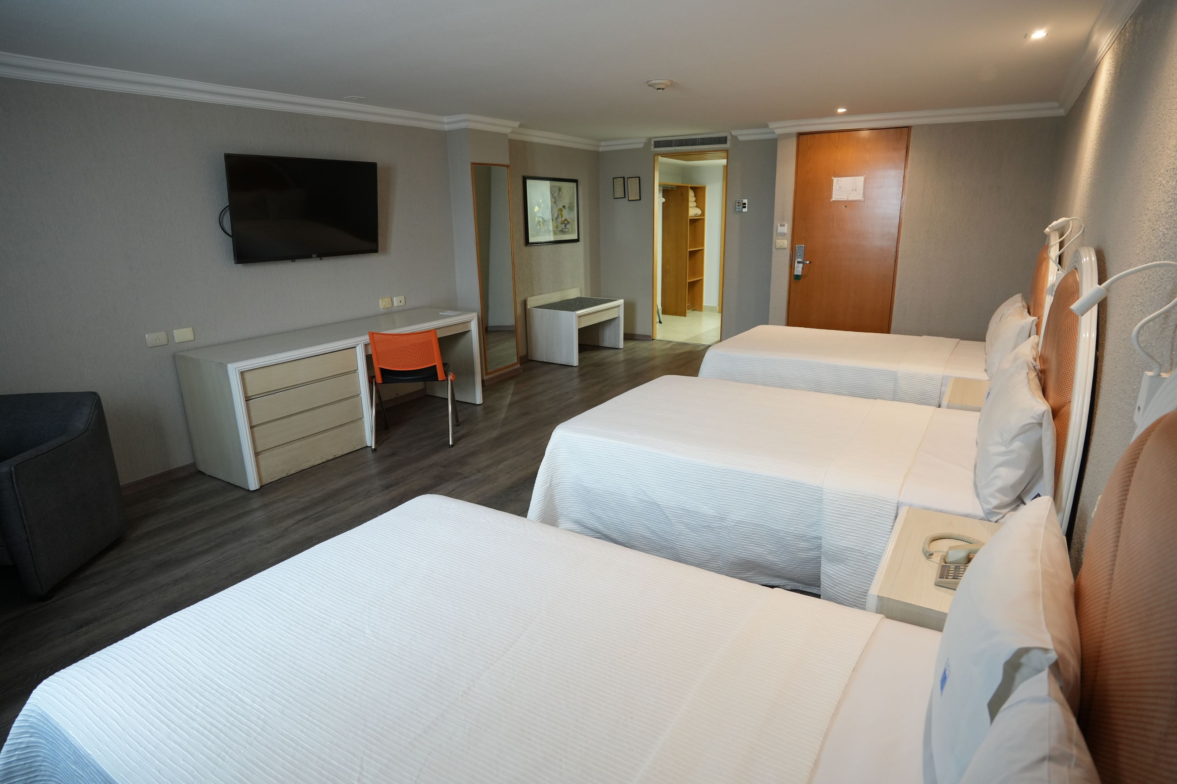A hotel room with two beds, a desk, a chair, a television, and a wardrobe.