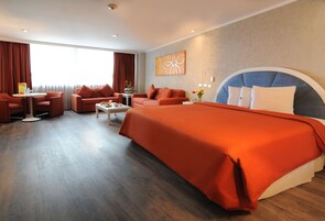 Una camera d'albergo con un letto grande, due divani, un tavolino da caffè e un piccolo tavolo con un vaso.