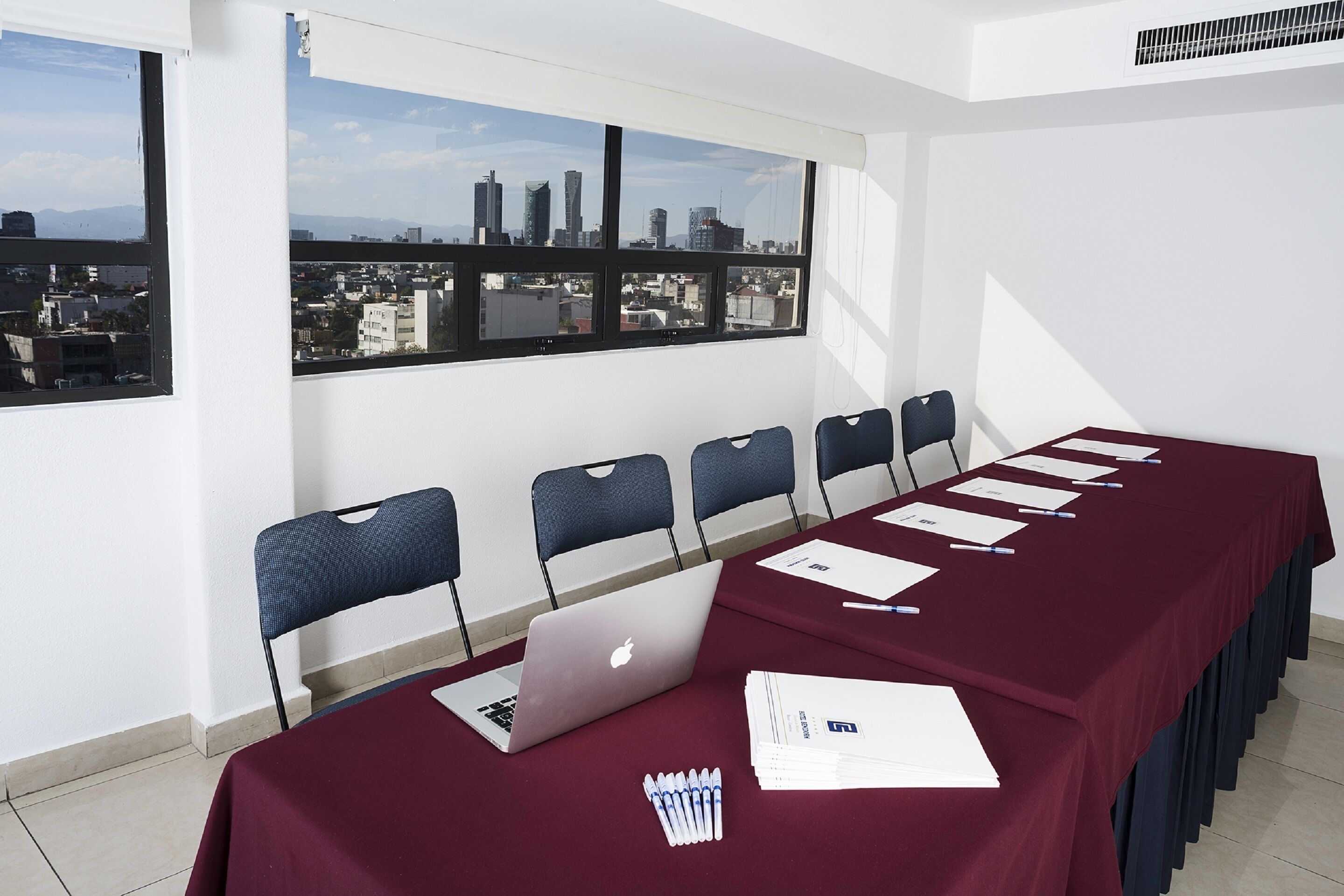 A conference room with a city view, a long table with chairs, and a laptop.