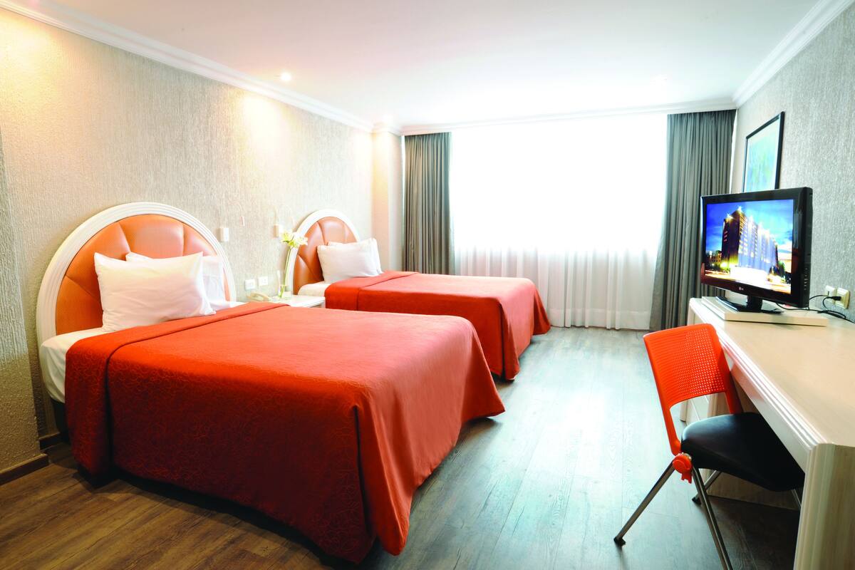 A hotel room with two beds, a desk with a chair, a television, and a window with curtains.