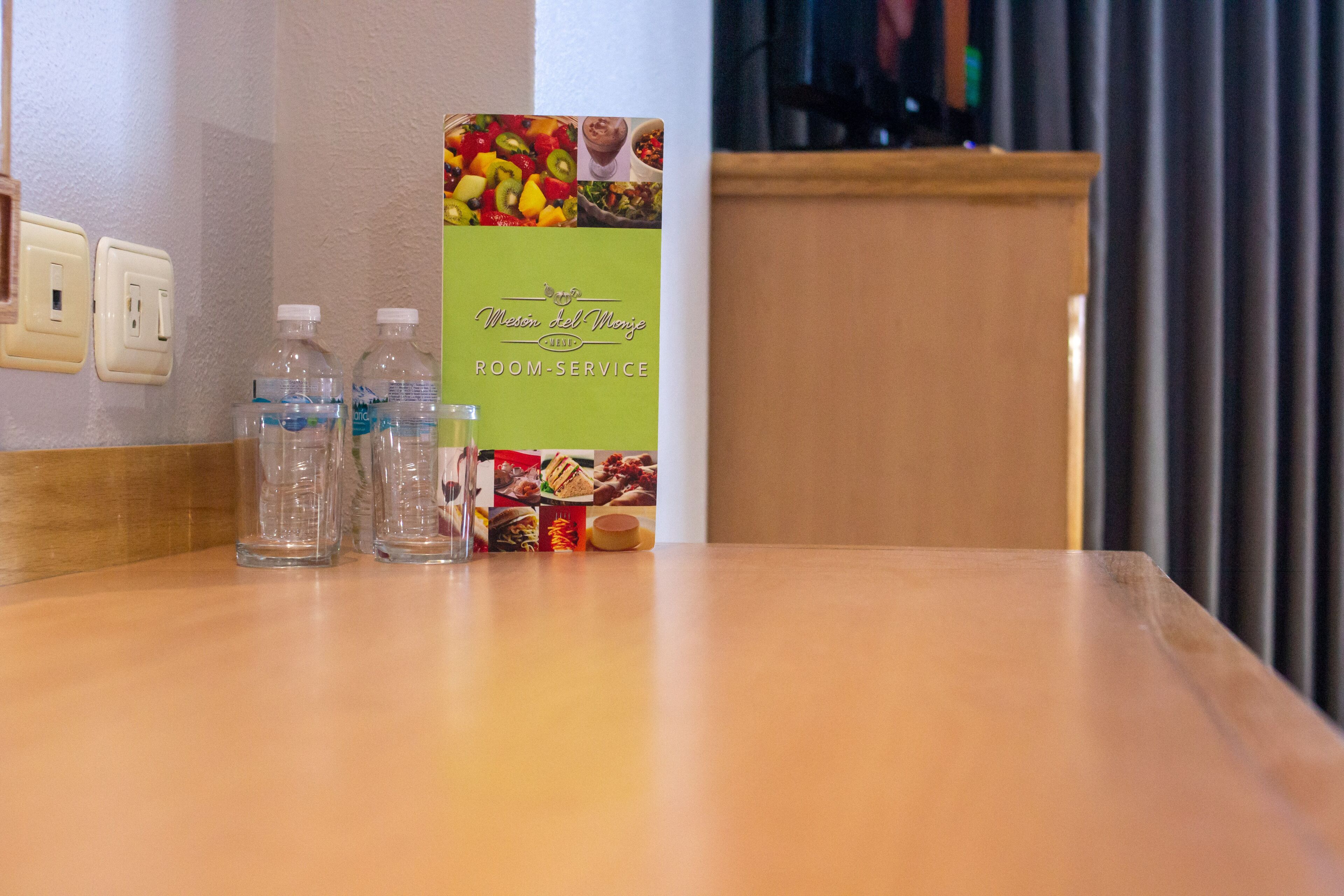 Ein Hotelzimmer mit Holztisch, zwei Wasserflaschen und einem Zimmerservice-Schild.