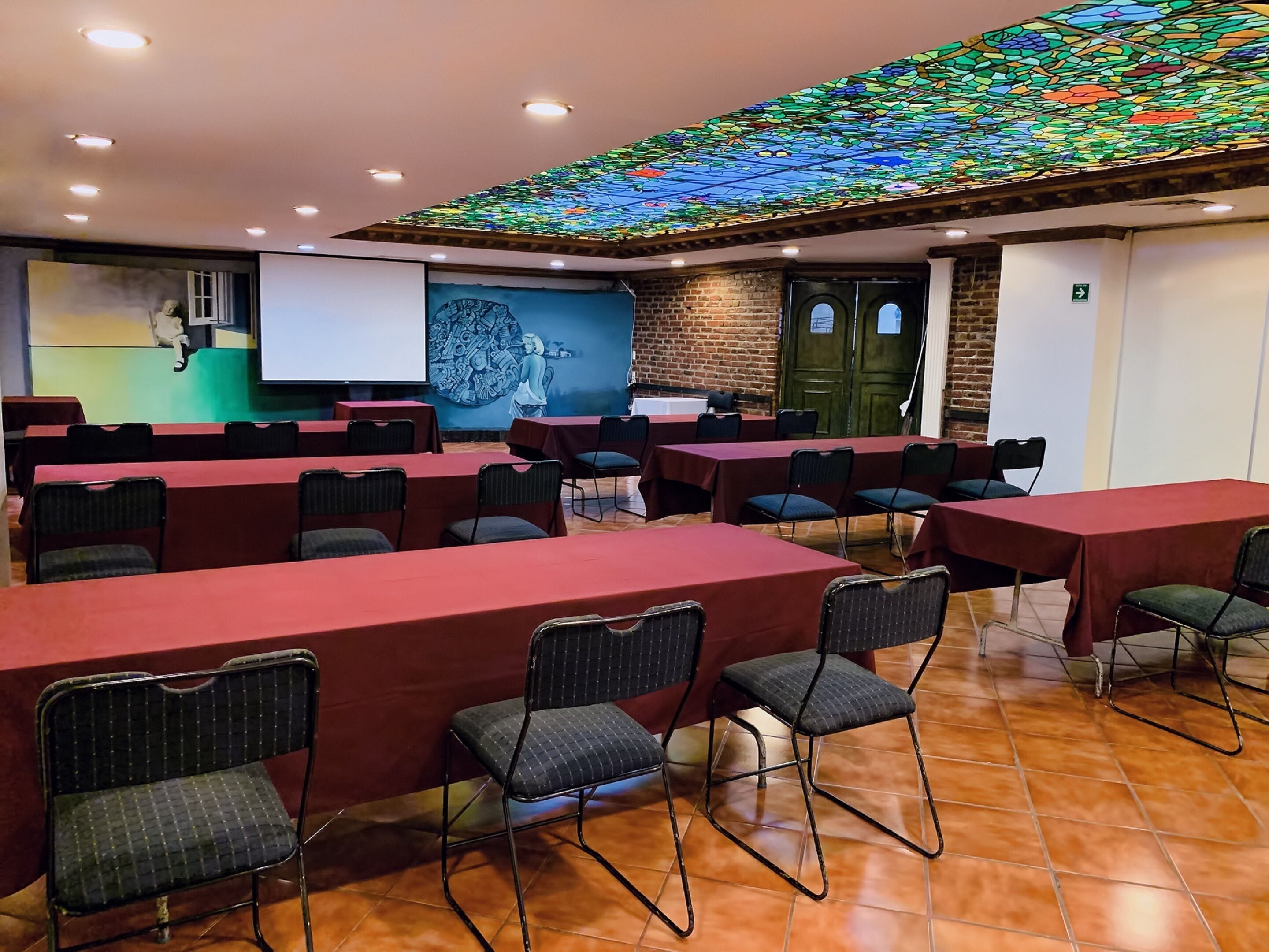 A conference room with tables and chairs, a projector screen, and a stained glass ceiling.