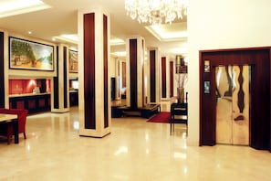 Enter a grand lobby with a polished floor, tall columns, and a beautiful painting above the reception desk.