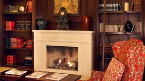 Una biblioteca con estanterías, chimenea y un sillón tapizado en rojo.