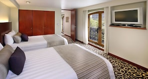 Two single beds with striped bedding and multiple pillows, a wardrobe, TV, and balcony with a decorative railing.